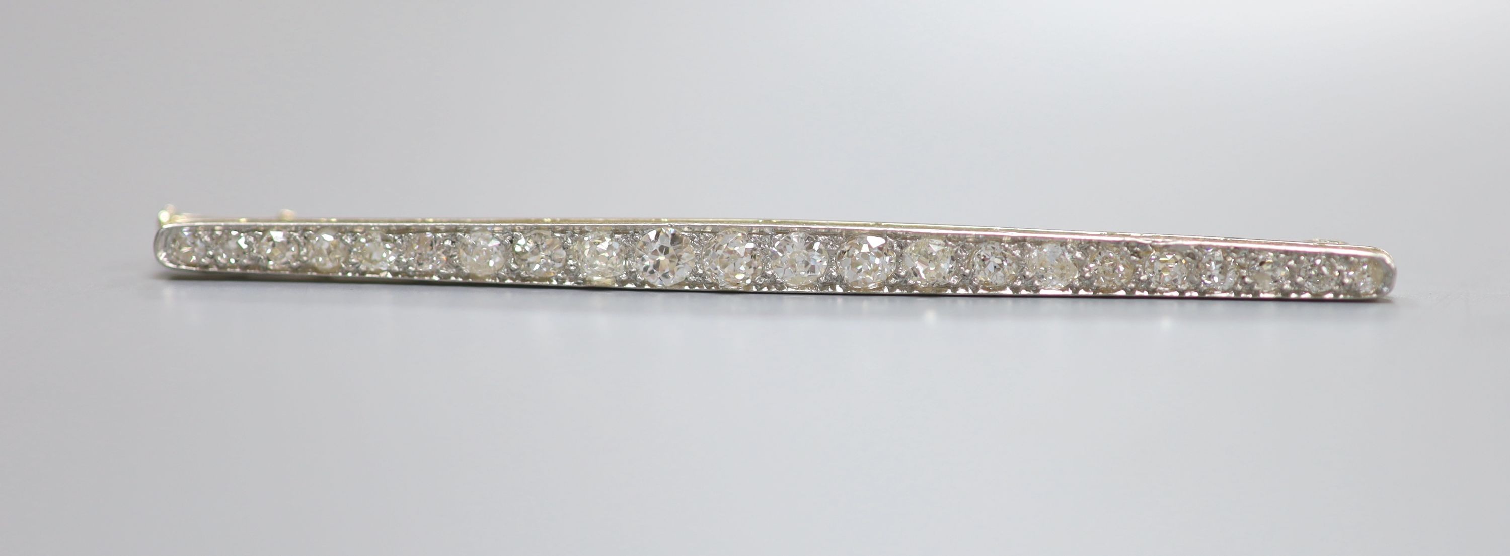 An early 20th century yellow metal and graduated twenty stone diamond set bar brooch, 67mm, 4.9 grams.